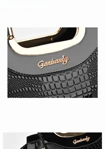 Detail of glossy black crocodile embossed leather handbag with premium gold hardware logo
