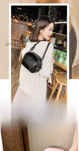 Detail of a black round leather crossbody bag with dual metal zippers and adjustable strap