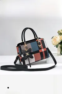 Detail einer karierten Handtasche mit Schmetterlingsanhänger und Metallkette