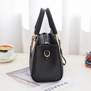 Large black leather tote bag with embroidery and gold hardware on a stylish white desk