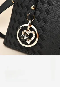 Detail of black woven leather handbag with gold heart pendant and enamel flower charm