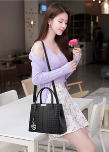 Close-up of black leather handbag featuring woven side panels and heart metal pendant