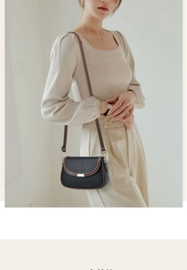 Detail of a black leather crossbody bag with crocodile texture and gold buckle on a model