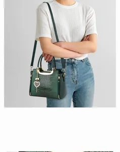 Detail of dark green crocodile texture handbag with gold metal handle and heart pendant