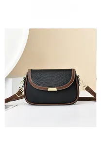 Detail of crossbody bag featuring black croc-embossed flap and gold metal buckle