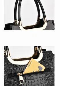 Detail of glossy black crocodile embossed leather handbag with golden metal handle