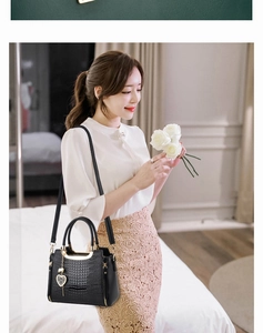 Detail of black crocodile texture handbag with heart-shaped charm and gold hardware