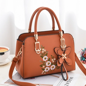 Caramel brown handbag with floral embroidery and butterfly charm shown in lifestyle setting