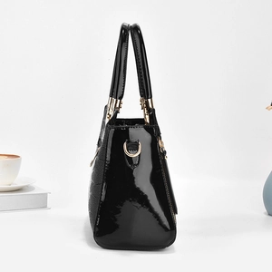 Classic black patent leather handbag with gold hardware on a minimalist background