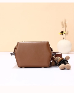 Brown leather crossbody bag with wide strap and teddy bear charm on white counter