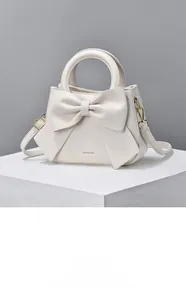 Detail of cream white leather handbag featuring a large 3D bow and golden hardware