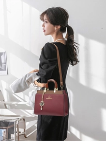 Burgundy contrast handbag with brown straps and golden cat pendant shown on a model