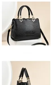 Dettaglio borsa nera texture coccodrillo con fibbie a cuore dorate e bordo superiore ondulato