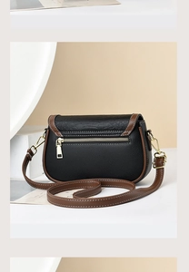 Detail view of the black pebbled leather crossbody bag with brown trim and gold zip pocket