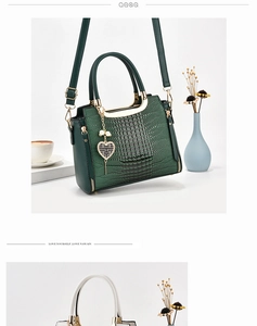 Detail of dark green crocodile embossed handbag with heart pendant and gold hardware