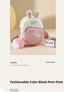 Detail view of mini pink crossbody bag featuring cute rabbit ears and fluffy pompom charm