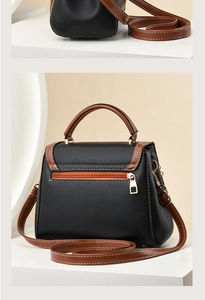 Detail view of black lychee grain leather crossbody bag with brown trim and back zipper pocket