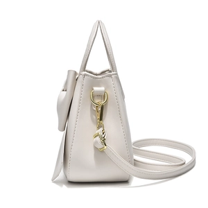 Creamy white trapezoid handbag with gold hardware and bow detail on white background