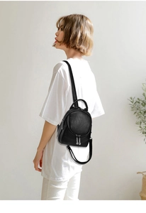 Detail of a minimalist black mini backpack with silver zippers worn by a model