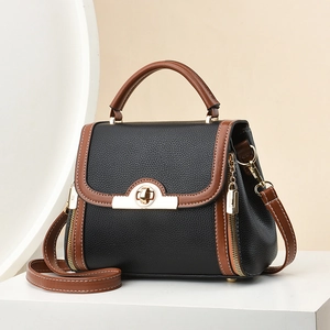 Fashion contrast crossbody bag with black lychee leather and brown trim on a white podium