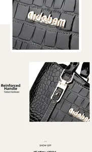 Detail of reinforced handles and golden metal logo on black crocodile texture handbag