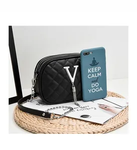 Three-layer black crossbody bag with V-shaped metal logo compared to iPhone for size reference