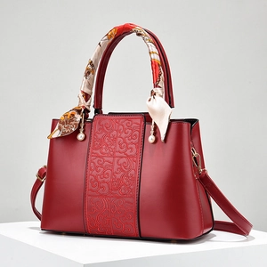 Elegant red leather handbag with embossed patterns, silk scarf handle, and pearl charms