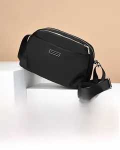 Close-up of black nylon crossbody bag with golden zippers and adjustable strap