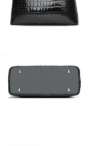 Detail of black crocodile-embossed patent leather bag showing back and metal protective feet