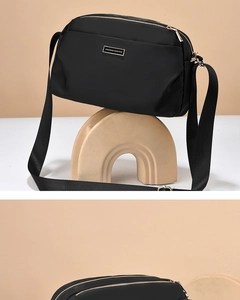 Close-up of black oxford crossbody bag featuring double zippers and metal nameplate