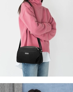 Close-up of black nylon crossbody bag with silver logo plate on pink knit sweater
