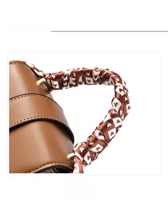 Detail of a brown leather handbag handle wrapped with a heart pattern printed silk scarf
