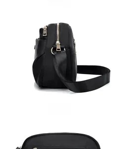 Detail view of black nylon crossbody bag featuring golden zippers and side pleated design