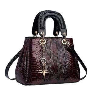 Fashionable snake-embossed burgundy handbag with dual handles and golden cross pendant
