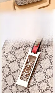 Detailed close-up of beige patterned handbag with red leather trim and gold hardware