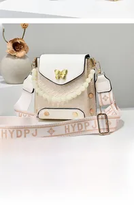 Detail of cream crossbody bag featuring a woven texture and golden butterfly clasp
