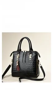 Detail of black crocodile texture handbag with gold hardware and tassel charm