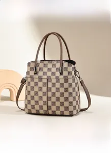 Detail view of checkerboard patterned bucket bag with brown leather handles and strap