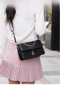 Outdoor shot of a black quilted leather crossbody bag with gold chain and printed strap