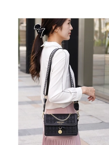 Detail of black quilted crossbody bag with patterned wide strap and gold chain