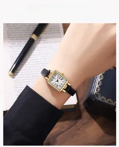 Detail of a vintage square watch with gold case and black leather strap worn on wrist