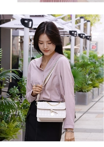 Detail of white quilted crossbody bag featuring gold chain strap and bow charm
