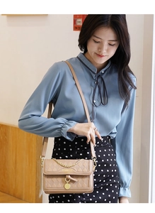 Detail of a khaki quilted chain shoulder bag paired with a light blue silk shirt