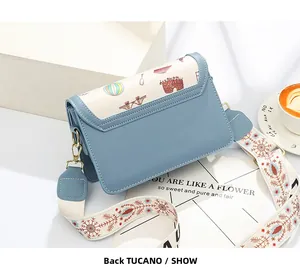 Detail of blue square flap bag with white stitching and colorful painted patterns