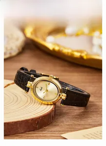 Detail of an oval vintage watch with gold case and black leather strap on a wooden surface