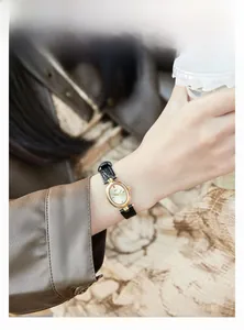 Close-up of vintage oval gold watch with black leather strap worn on a female wrist