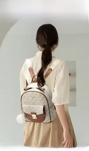 Fashionable mini backpack with MK monogram print and fluffy white ball charm on model
