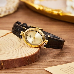 Vintage gold oval quartz watch with black leather strap on a rustic wood stand