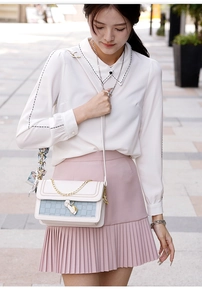 Detail of white and blue crossbody bag with woven texture and gold heart pendant