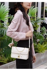 White quilted crossbody bag with golden chain and floral scarf accessory shown on model